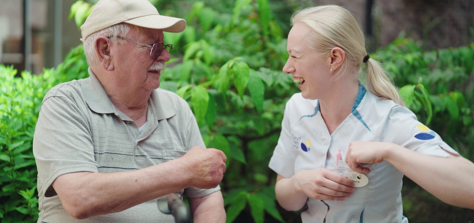 Zorgmedewerker en bewoner lachen samen in de tuin, een beeld uit de employer brand video