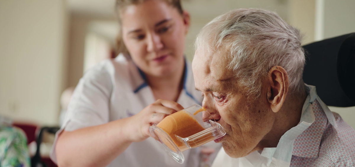 Zorgondersteuner van Land van Horne helpt een bewoner met drinken aan tafel