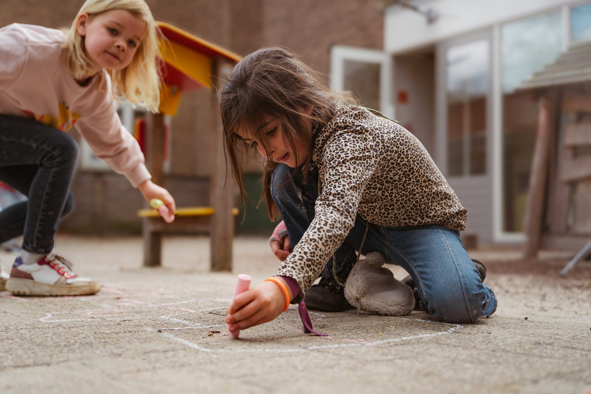 Twee meisjes tekenen met stoepkrijt op het plein van de BSO