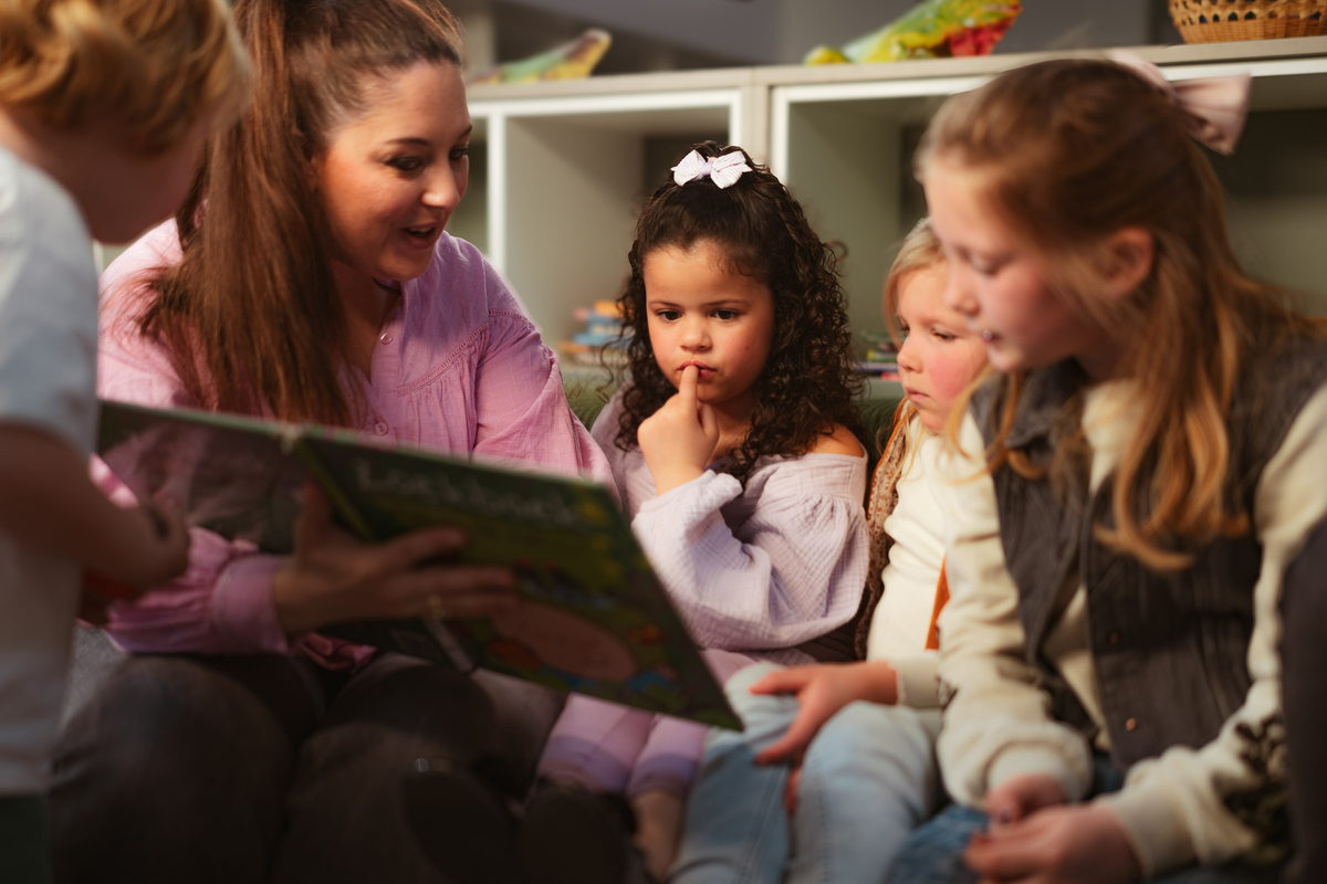 Pedagogisch professional leest voor aan een groepje kinderen op de bank